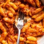 A bowl of malloreddus pasta tossed in a tomato butter sauce with a fork.