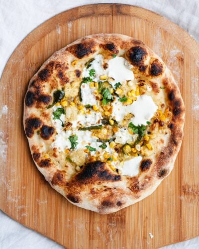 A corn and mozzarella pizza sitting atop a wooden pizza peel.