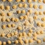 Handmade orecchiette pasta on a baking sheet dusted with semolina flour.