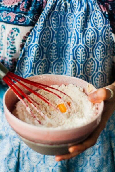 Person in apron whisking a bowl of flour.