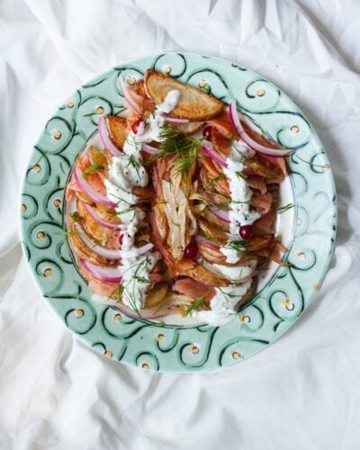 A decorative plate with layers of smoked salmon, potato, red onion, and a yogurt sauce drizzled over the top.