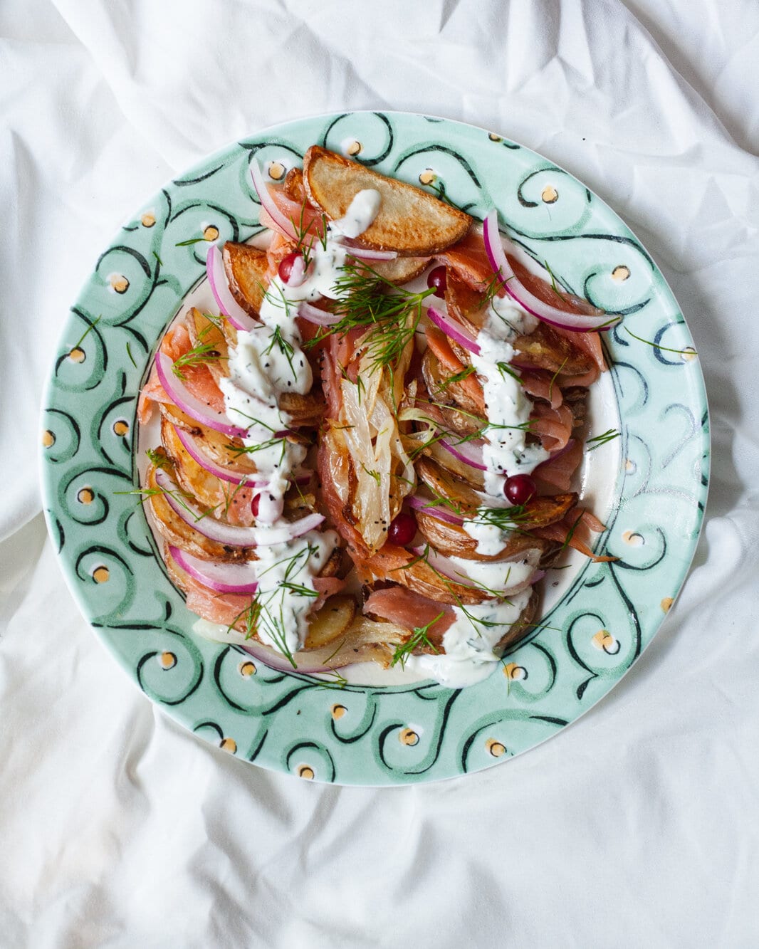 A decorative plate with layers of smoked salmon, potato, red onion, and a yogurt sauce drizzled over the top.