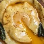 An egg yolk streaming out of a raviolo in a brown butter sauce with crispy sage.