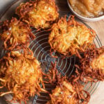 Crispy potato latkes set atop a wire rack with applesauce in the background.