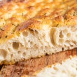 A loaf of focaccia cut in half with a slice on the side.