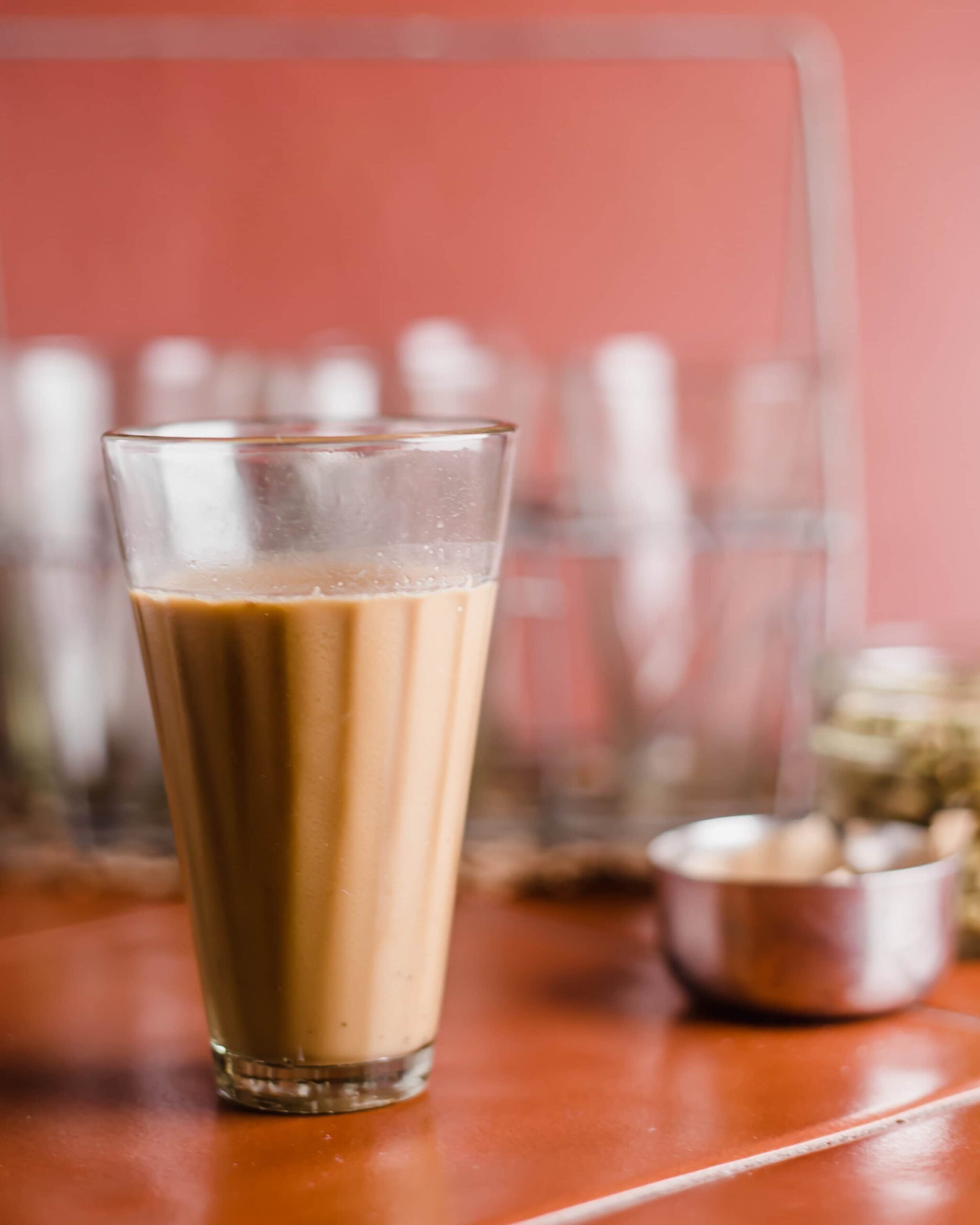 A glass of chai with more glasses and spices in the background.