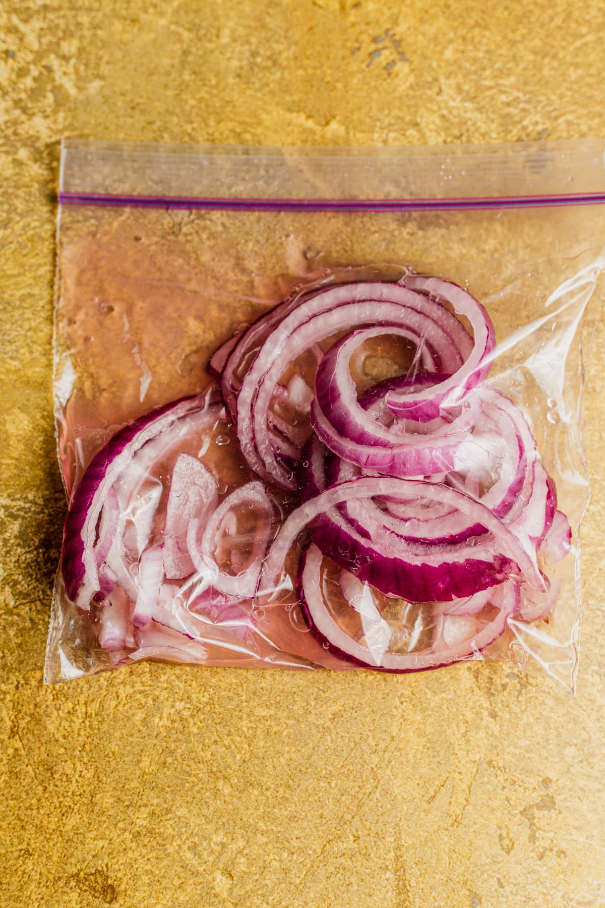 Ziploc bag with rings of red onion marinating in lie juice.