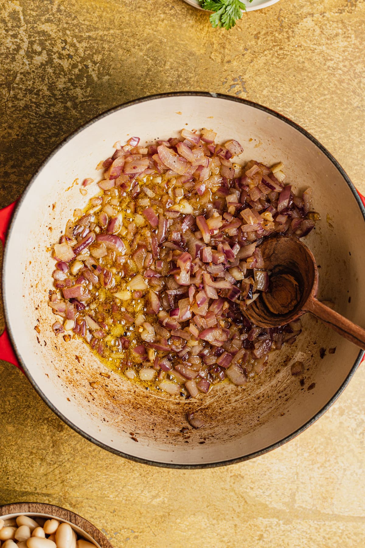 Sauteed red onion in a skillet with a wooden spoon.