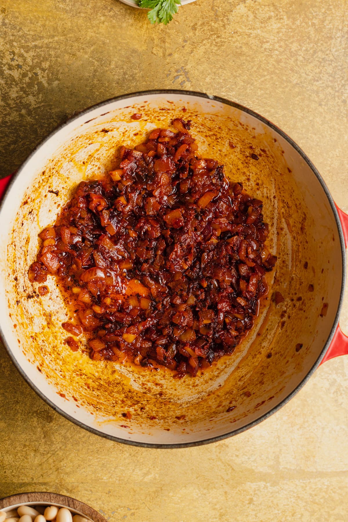 Caramelized tomato paste and onion in a skillet with some paste stuck to the sides of the pan.