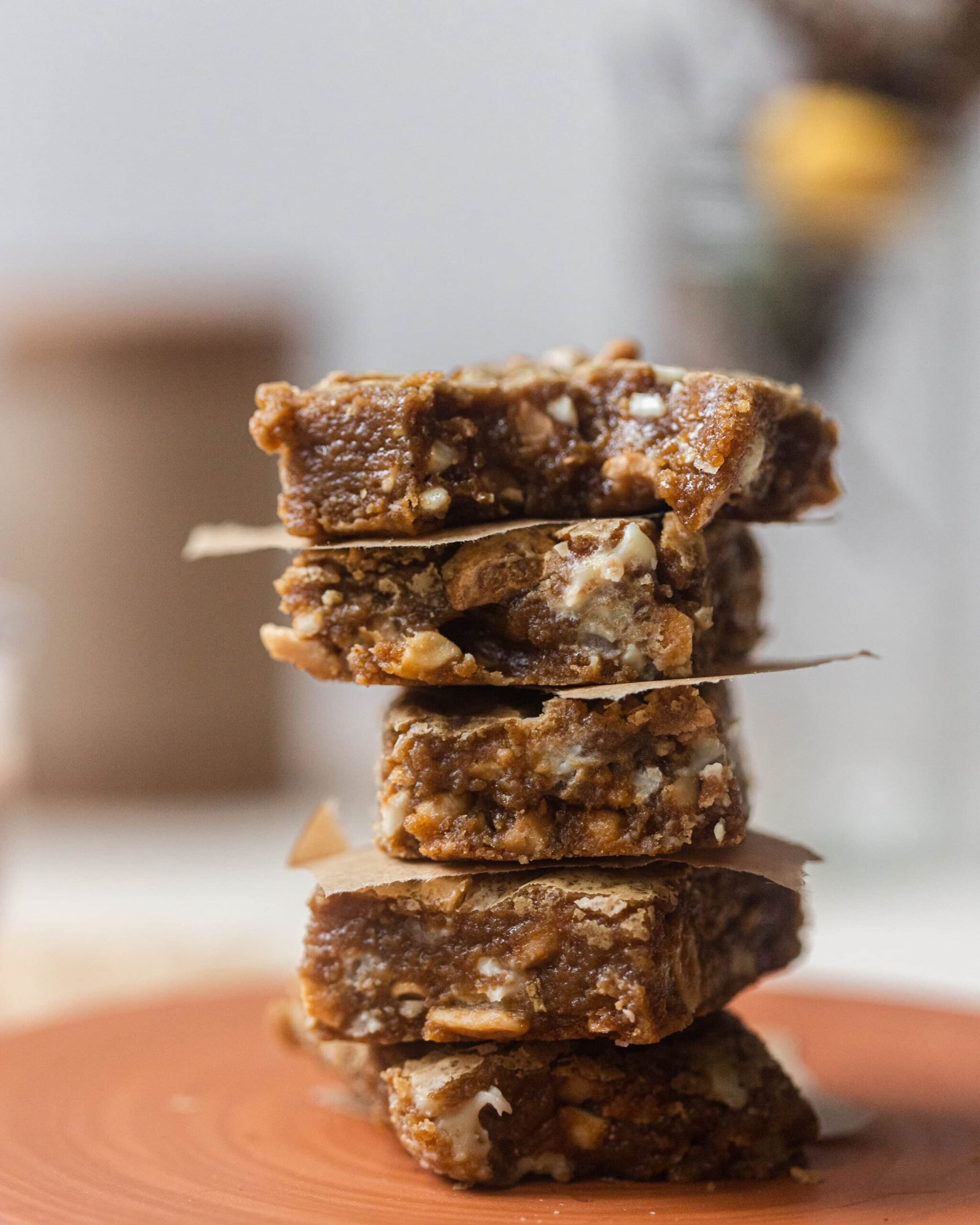 A stack of blondies with the top one with a bite taken out of it on a terracotta plate.
