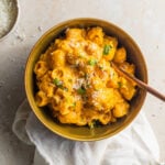 Bowl of creamy pumpkin pasta with herbs and cheese on top.
