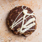 Cocoa sable cookie with hazelnuts and a white chocolate glaze on a countertop.