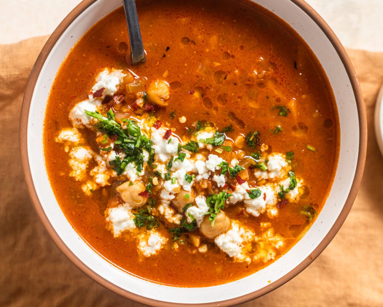 Bowl of chickpea pepper soup with feta and herbs.