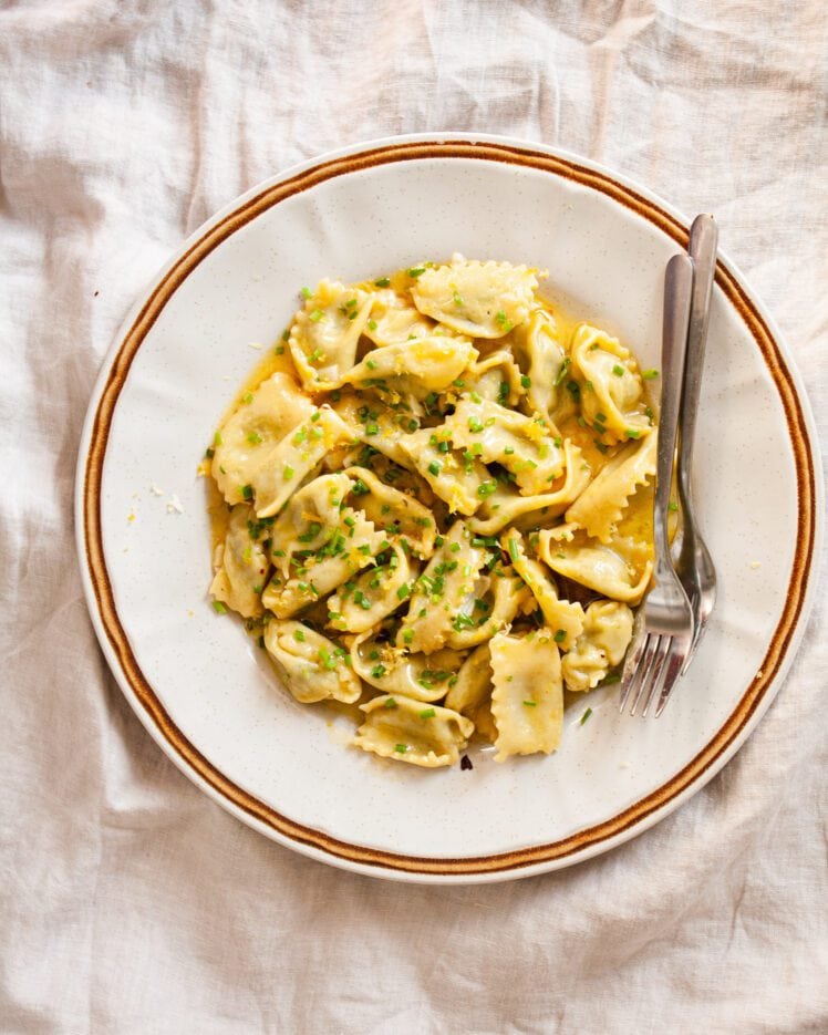 A plate of agnolotti tossed in a butter sauce with two forks next to it.