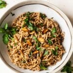 A bowl of maggi noodles with herbs, garlic, and sesame seeds on top.