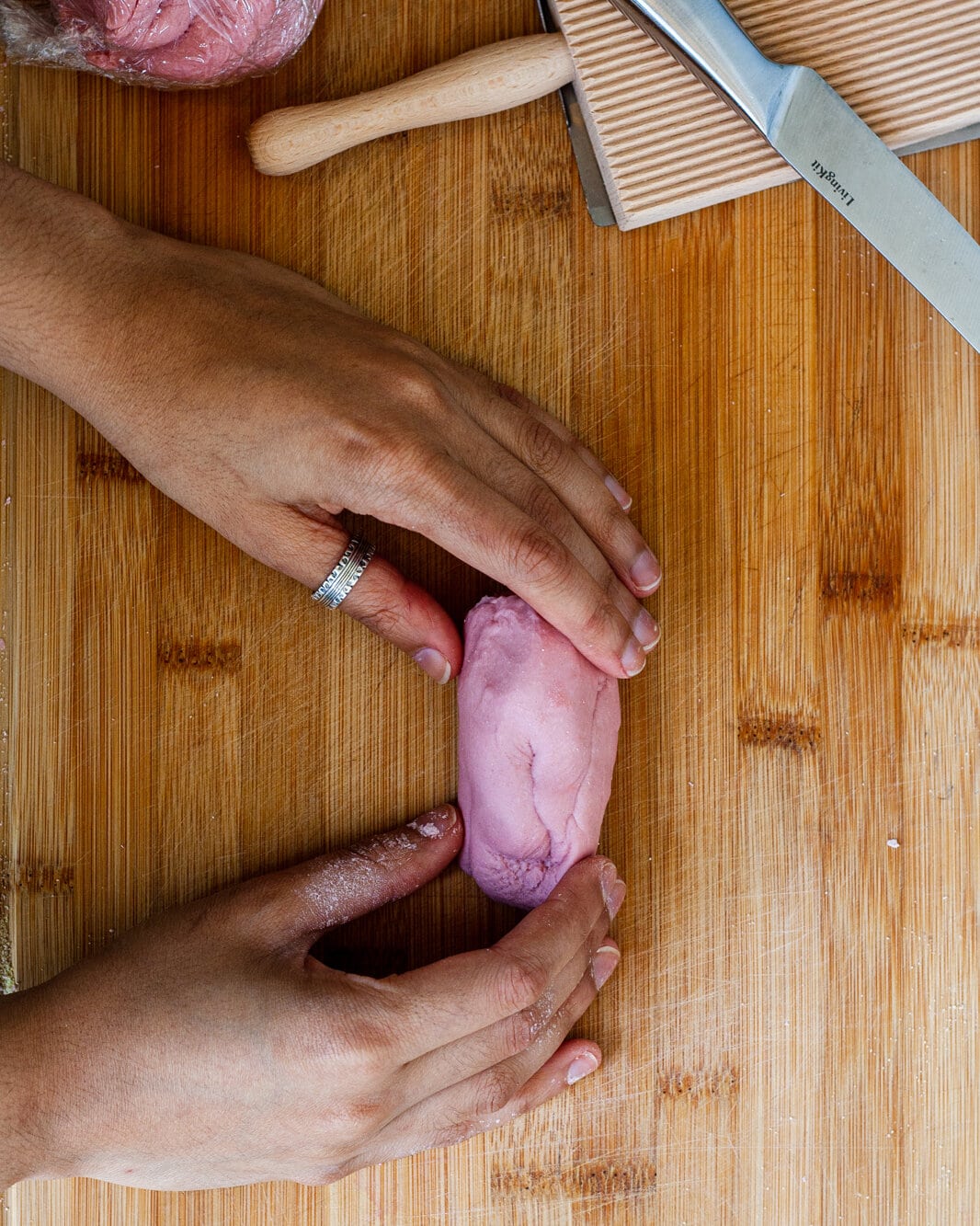 Hands holding pink dough on a cutting board.