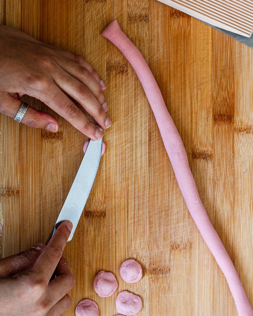 Hand scraping a piece of pasta dough with a knife.