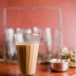 A glass of masala chai with more glasses and cardamom pods in the background.