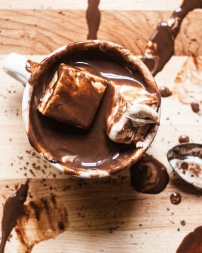 A mug of hot chocolate with fluffy marshmallows on a chocolate spattered cutting board.