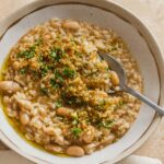 A bowl of risotto topped with white beans and fresh herbs.