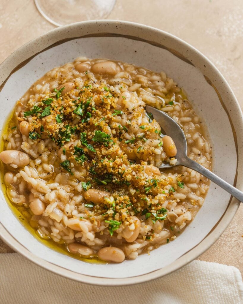 A bowl of risotto topped with white beans and fresh herbs.