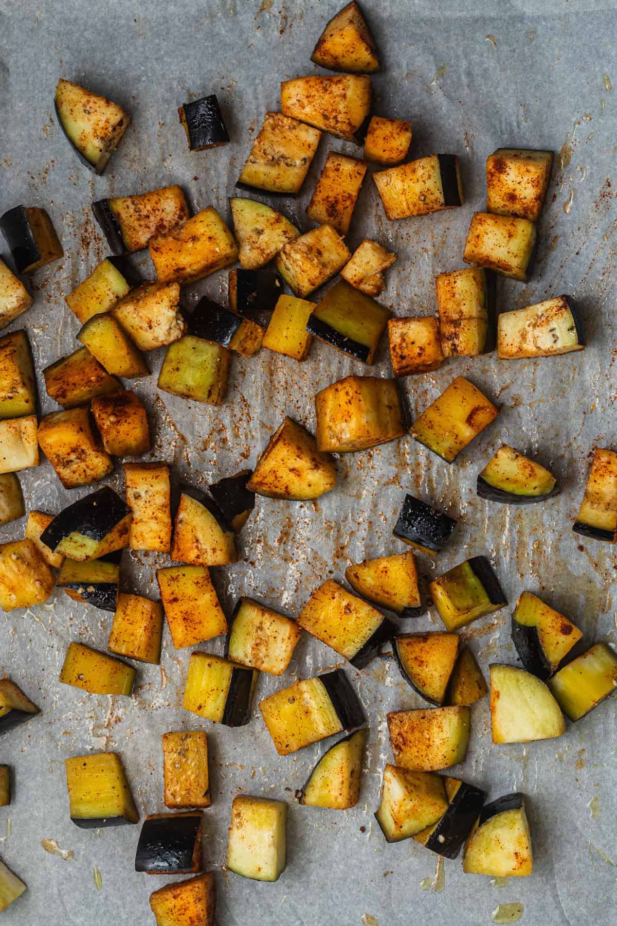 Cubes of eggplant tossed in spices on a parchment-lined baking sheet.