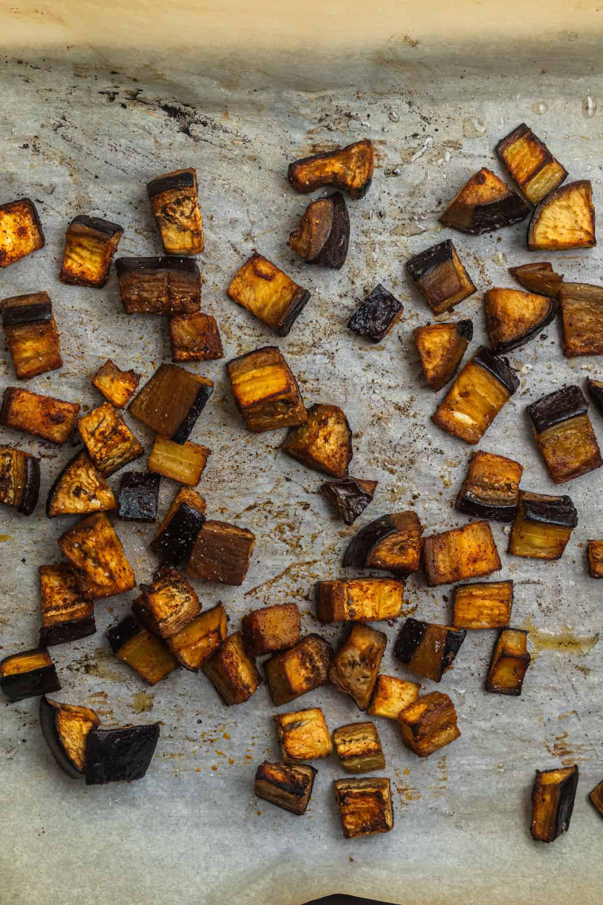 Roasted eggplant cubes on a parchment-lined baking sheet.