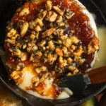 A cast-iron skillet filled with melted baked brie topped with jam and nuts.