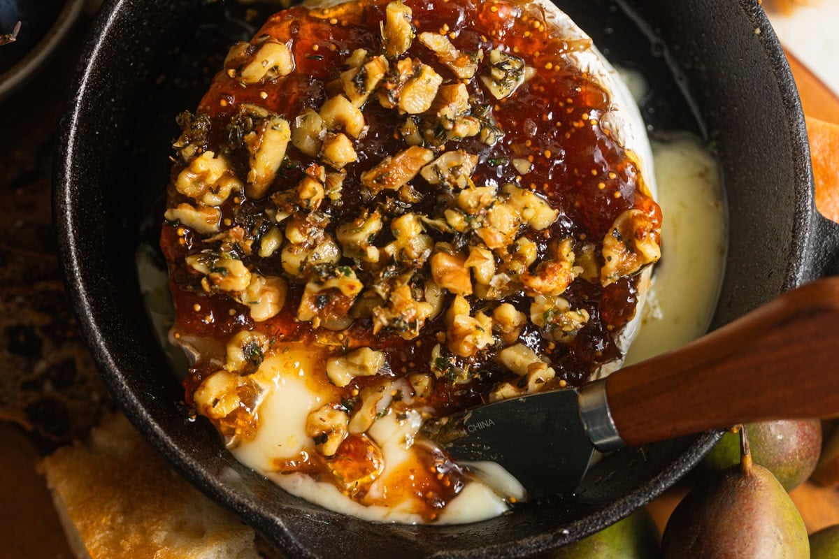 A cast-iron skillet filled with melted baked brie topped with jam and nuts.