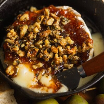 A cast-iron pan with melting brie topped with jam and pistachios.