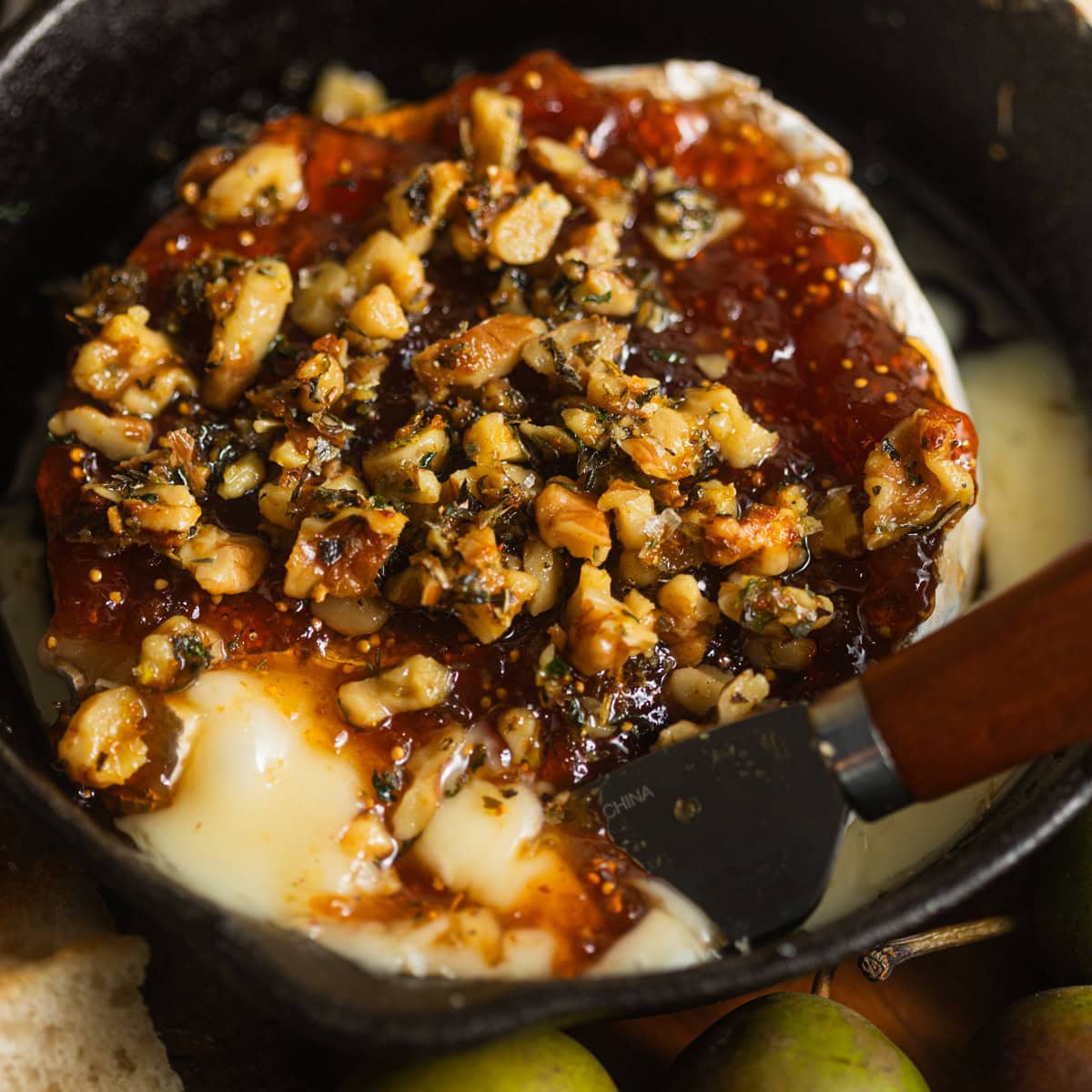 A cast-iron pan with melting brie topped with jam and pistachios.