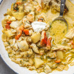 A bowl of crab stew with potatoes, fish, and other vegetables, topped with a dollop of yogurt.