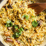 Mushroom biryani with cilantro in a pot with a wooden spoon.