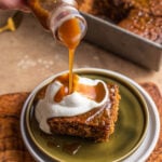 Drizzling toffee sauce over a plate of sticky toffee pudding with whipped cream.