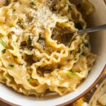 Mafaldine twirled with a fork in a serving bowl dusted with parmesan cheese.
