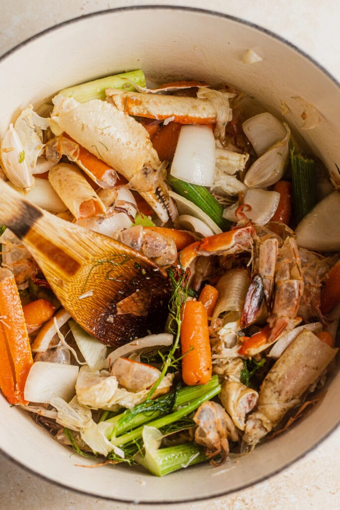 Dutch oven with a wooden spoon, seafood shells, and aromatics.