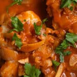 Cod in a tomato sauce topped with fresh parsley and various cooked alliums.
