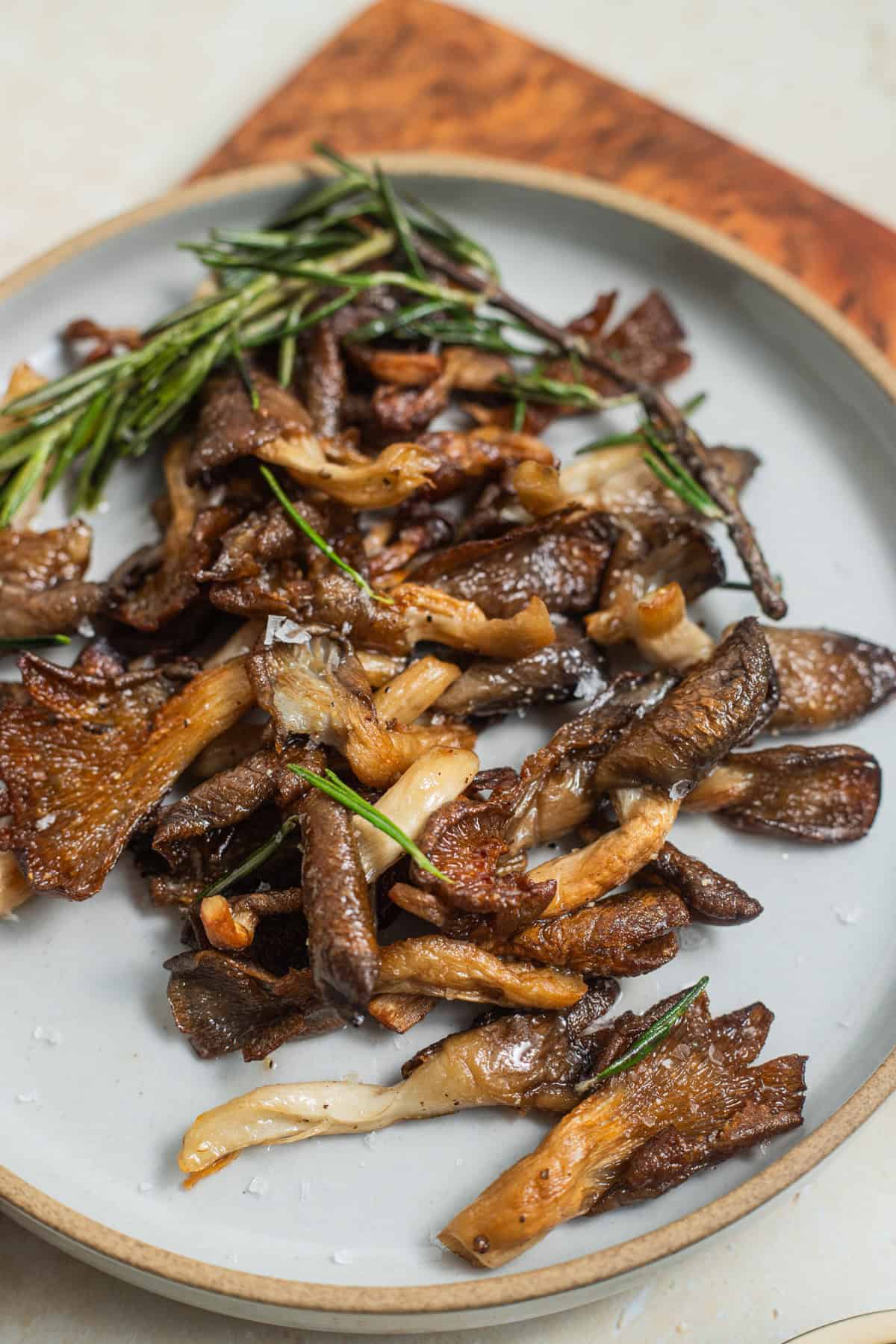 A plate of crisped up oyster mushrooms with sprigs of rosemary and flaky salt on top.