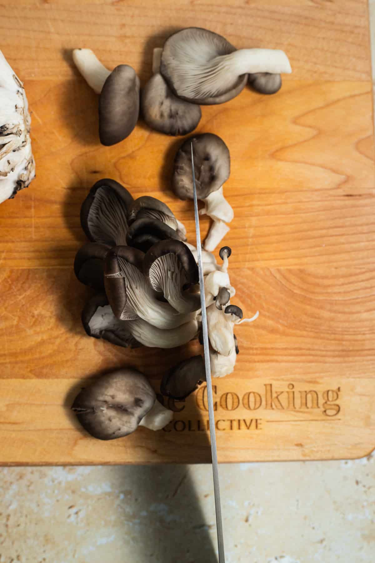 A knife cutting through a cluster of oyster mushrooms on a cutting board.
