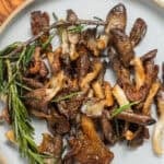 A plate of crispy sauteed oyster mushrooms topped with a sprig of rosemary and flaky salt.
