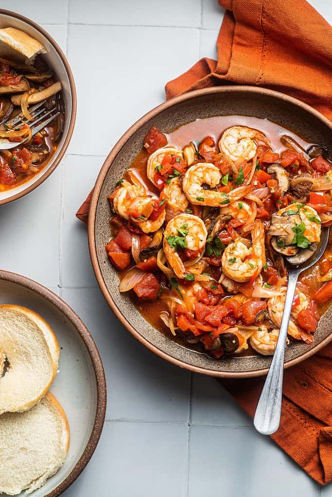 A bowl of shrimp cacciatore with a bowl of bread next to it.