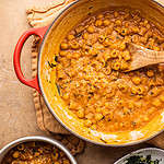 A dutch oven with a stew of chickpeas and pasta with a wooden spoon in it.