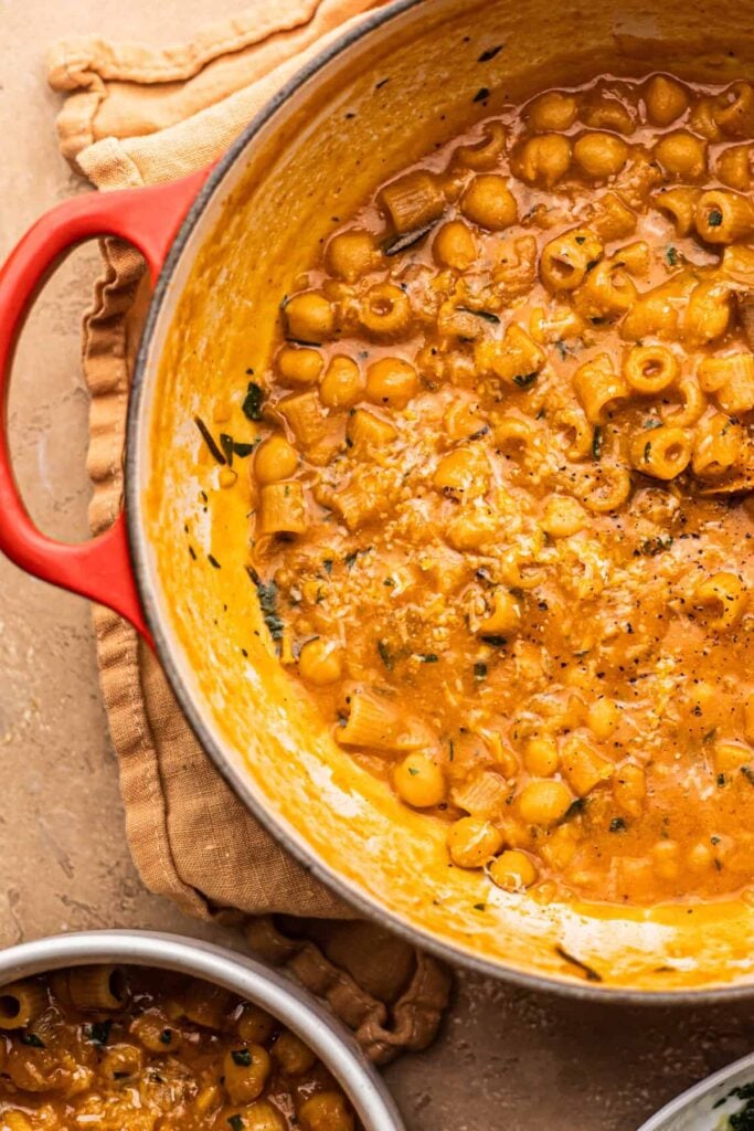 A dutch oven with a stew of chickpeas and pasta with a wooden spoon in it.
