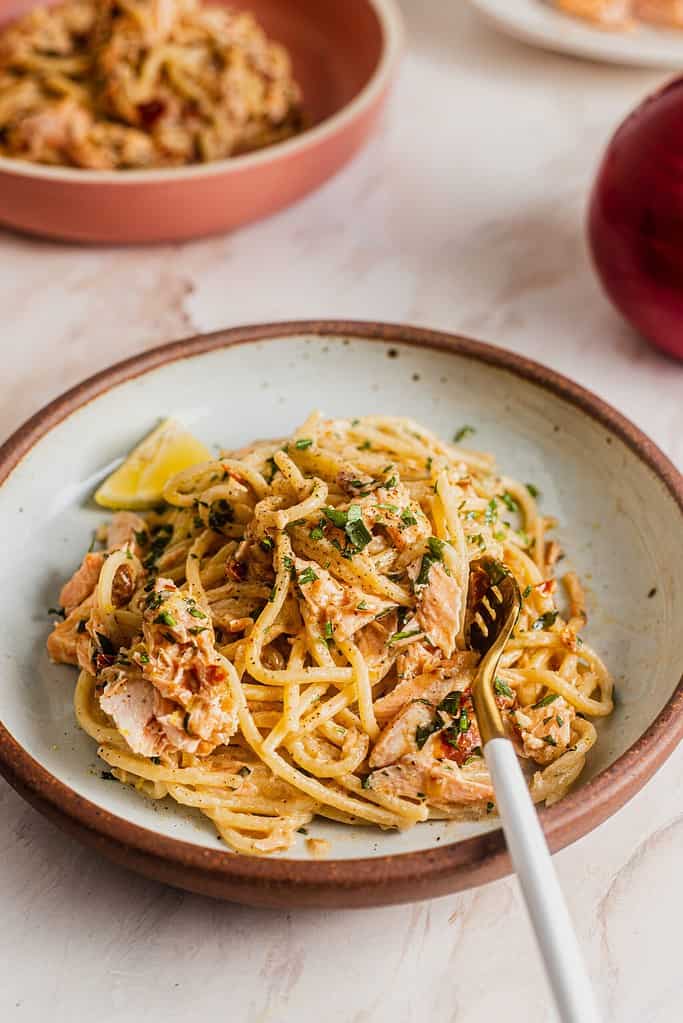 A plate of salmon pasta with another bowl in the background.