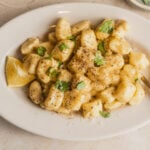 Plate of ricotta gnocchi with black pepper, herbs, and a lemon wedge.