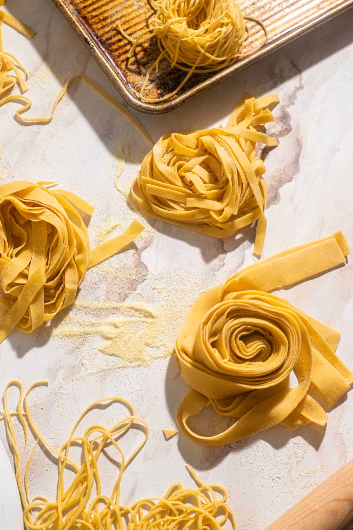 Nests of pasta dough of various sizes on a marble board.