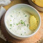 Sour cream and chive dip in a bowl with a chip inside.