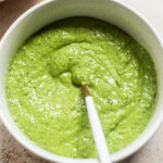 Bowl of speckled avocado green goddess dressing with a spoon in it.