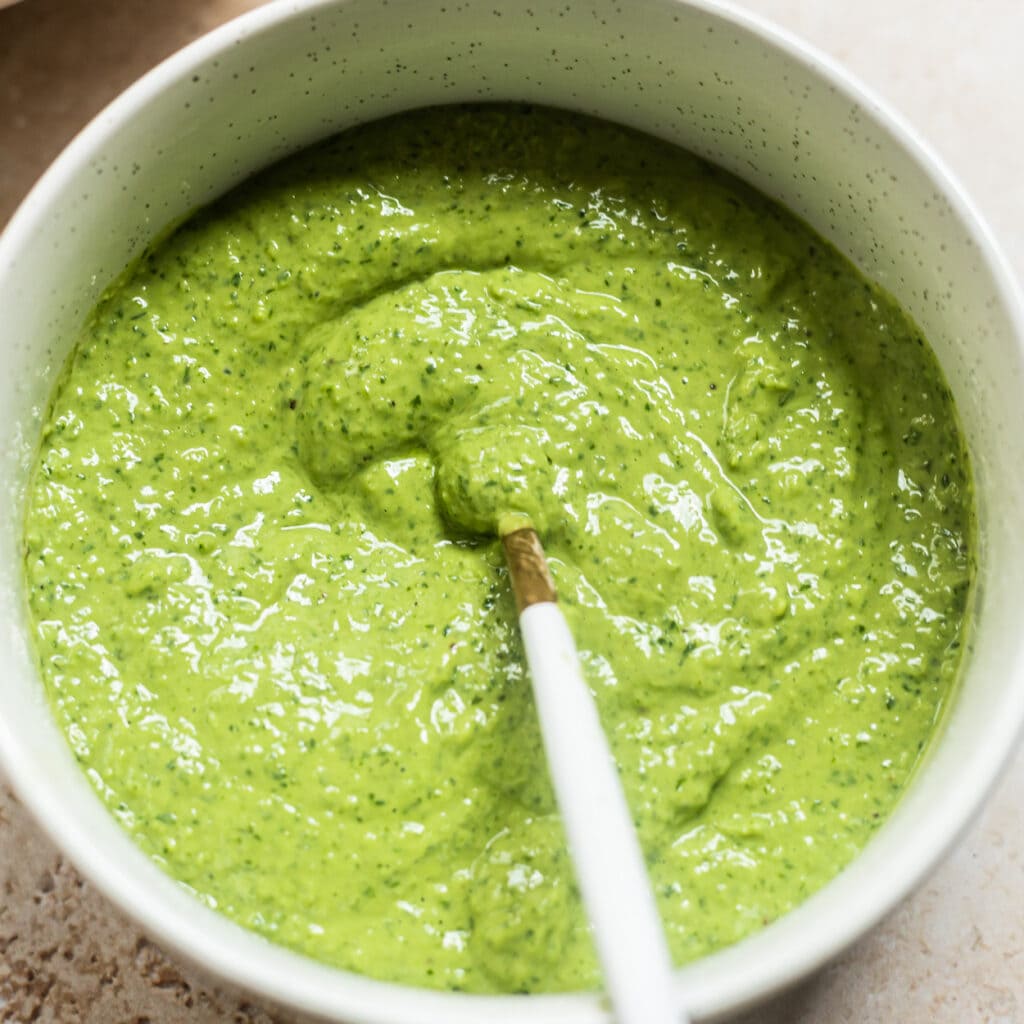 Bowl of speckled avocado green goddess dressing with a spoon in it.