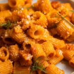 A plate of pasta tossed with tomato sauce topped with fennel fronds and cheese.